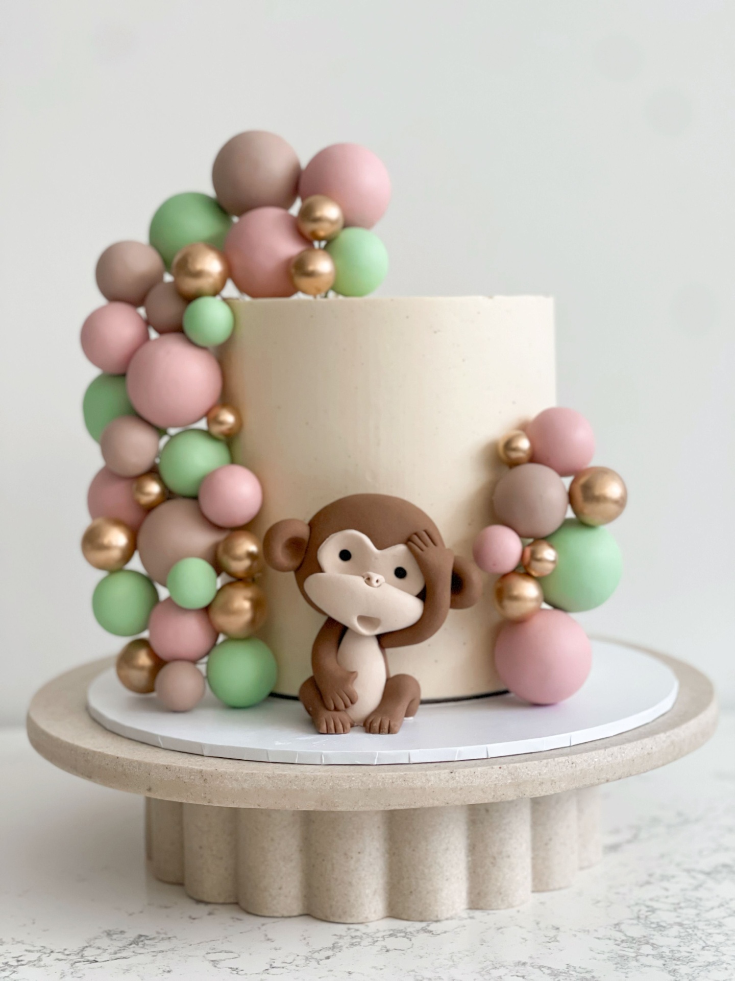 Cream cake with fondant monkey topper and pink, green and gold sphere garland